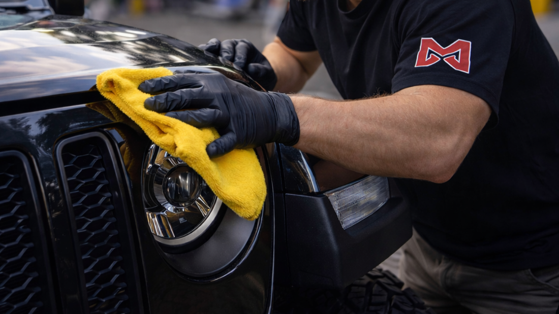 Professional auto detailer polishing a black Jeep headlight inside a detailing shop with blurred workshop background.